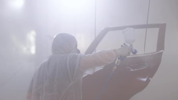 Processo de pintura spray industrial. Auto pintor pulverizando tinta vermelha na porta do carro em cabine especial. Pintura de peças de veículos na oficina de serviço de carro. Técnico masculino é ar-pintura carros porta — Vídeo de Stock