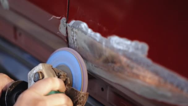 Primer plano del trabajador muele daños en el coche. El rectificado duro está diseñado para suavizar las irregularidades. Trabajador profesional taller de automóviles muele la puerta abollada del coche — Vídeos de Stock