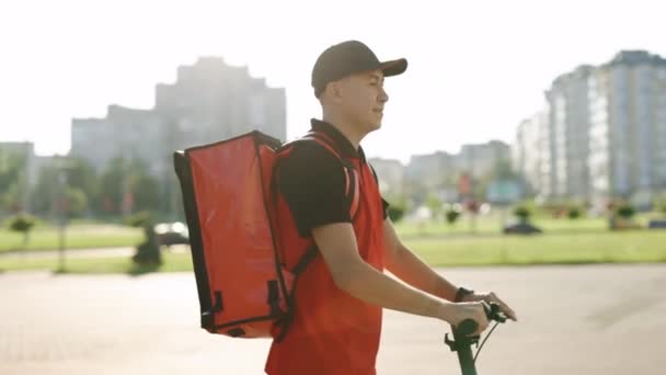Курьер-мужчина с изотермическим рюкзаком коробка для пиццы едет на электрическом скутере вдоль стены в городском стиле. Экспресс-доставка еды из кафе и ресторанов — стоковое видео
