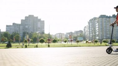 Kırmızı sırt çantalı bir teslimatçı elektrikli scooterla videoda beliriyor ve baş parmağını kaldırıyor. Mükemmel atış. Ekolojik alternatif ulaşım