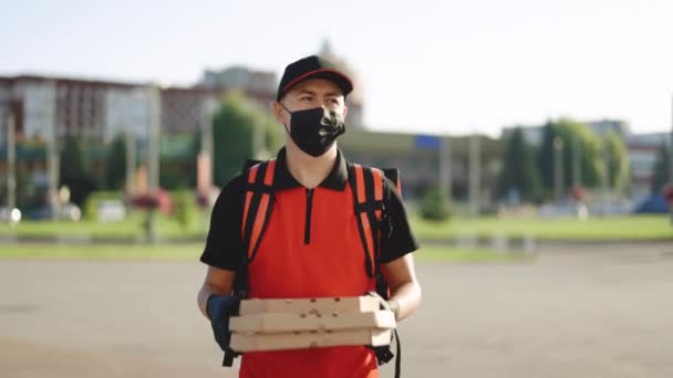Joven mensajero de comida masculina con máscara protectora mientras camina por la calle de la ciudad con una mochila roja aislada que entrega el orden. Servicios de entrega. Excelente entrega — Vídeo de stock