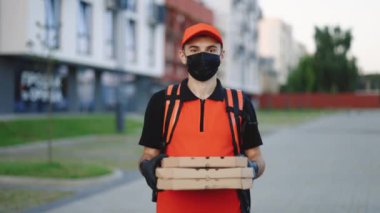 Karton kutularda pizza taşıyan, koruyucu maske ve eldiven takan kırmızı sırt çantalı kurye adam portresi. Mükemmel atış. Teslimat hizmetleri