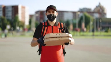 Karton kutularda pizza taşıyan, koruyucu maske ve eldiven takan kırmızı sırt çantalı kurye adam portresi. Teslimat servisi. Mükemmel atış.