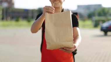 Mutlu teslimat işçisi elinde paketle kameraya bakıyor ve gülümsüyor. Pozitif genç kurye portresi. Kapıdan kapıya servis servisi.