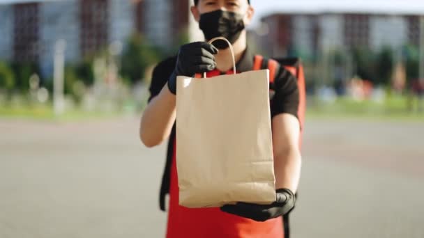 Yiyecek teslimatçısı elinde yiyecek dolu bir poşet tutuyor koruyucu maske eldivenli teslimatçı, koronavirüs COVID-19 salgını karantina salgını. Teslimat hizmetleri — Stok video