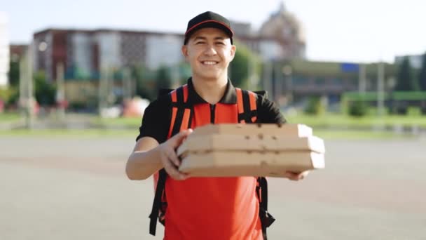 Asiatisk budbringer arbejder i uniform med rød termisk pizza rygsæk om aftenen. Postbud og ekspreslevering af dagligvarer koncept. Fast food bekvemmelighed levering og transport – Stock-video