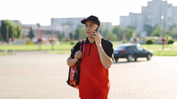 Food delivery guy with red backpack deliver orders. Male courier with isothermal food case box arrives to the entrance to the house and calls for client — Stock Video