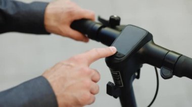 İş adamının elleri elektrikli scooter 'ı çalıştırıyor. Erkek, şehrin caddesinde modern aletin başlama düğmesine basıyor. Ekolojik alternatif ulaşım. Çevre dostu ulaşım