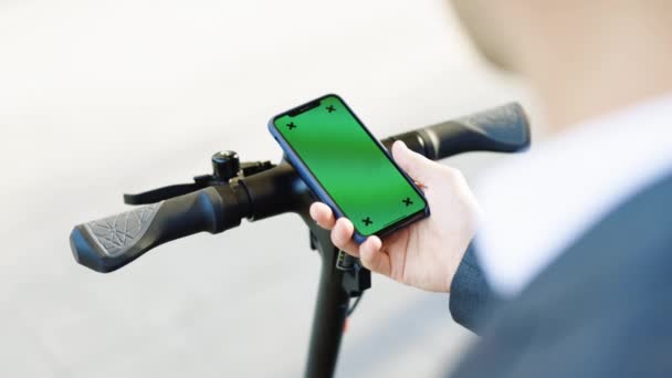 Kromakey akıllı telefon ekranıyla elektrikli scooter elin yakın çekimi. Turist yeşil ekranlı telefon kullanıyor cep telefonu uygulaması kullanarak elektrikli scooter kiralıyor. Çevre dostu ulaşım — Stok video