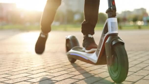 Modern Adam Güneşli Gün 'de elektrikli scooter kullanıyor. İşe elektrikli scooterla giden yetişkin bir adam. Siyah spor ayakkabılı adam elektrikli mobiletle geziyor. Çevre dostu ulaşım — Stok video