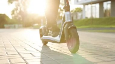 Modern yollarla işe giderken elektrikli scooter kullanan siyah ayakkabılı hippi bacaklar. Hızlı sürüşlü elektrikli taşıma. E-scooter sürücüsü, insan sürüşü paylaşımı veya kişisel çevre taşımacılığı