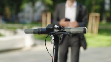 Klasik takım elbiseli tanınmamış bir işadamı elektrikli scooter 'a doğru geliyor ve cep telefonu uygulaması kullanıyor. Adam elektrikli scooter kiralıyor. Çevre dostu ulaşım. İş merkezinin açıkları.
