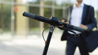 Takım elbiseli tanınmayan bir işadamı elektrikli scooterın yanına geliyor. Kiralık scooter için telefon başvurusu. Ekolojik şehir ulaşımı. İş adamı cep telefonu uygulaması kullanarak elektrikli scooter kiraladı