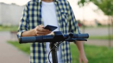 Kiralık scooter için telefon başvurusu. Akıllı telefonlu bir adama yakın çekim. Bisiklet ya da e-scooter kullanan bir turist. Ekolojik şehir ulaşımı. E-scooter sürücüsü kirada kişisel eko taşımacılık