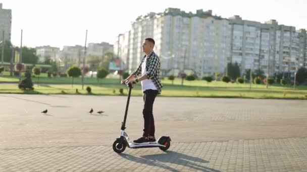 Självsäker trendig ung man i skjorta kommer att arbeta rida på moderna transporter elektrisk skoter. Snygg affärskille som kör scooter på gatan på morgonen. Ekologi och stadsliv — Stockvideo