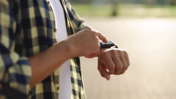 Un reloj inteligente. Reloj inteligente en una mano de hombre al aire libre. Mano de hombre tocando un reloj inteligente. De cerca - hasta tiro de machos usos de la mano de reloj inteligente portátil al aire libre. — Vídeos de Stock