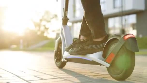 Foot 'u kapatın kurye yemek teslimatı elektrikli scooter' la yolda gidiyor günbatımında internetten sipariş veren müşteriyi teslim ediyor. Siyah spor ayakkabılı genç adam elektrikli mobilete biniyor. — Stok video