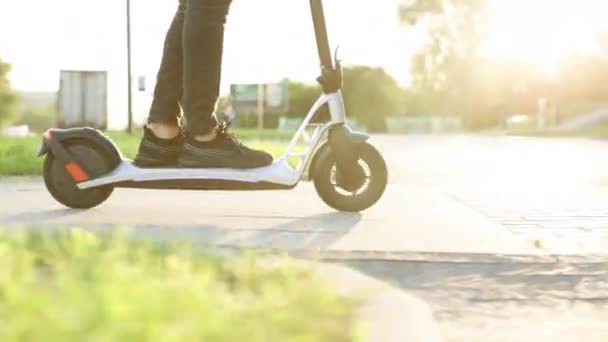 Sköt på ben ung man i svarta sneakers rida på elektrisk mobil skoter. Närbild fötter man kurir mat leverans rider på gatan på elektrisk skoter leverera online beställning klient vid solnedgången — Stockvideo