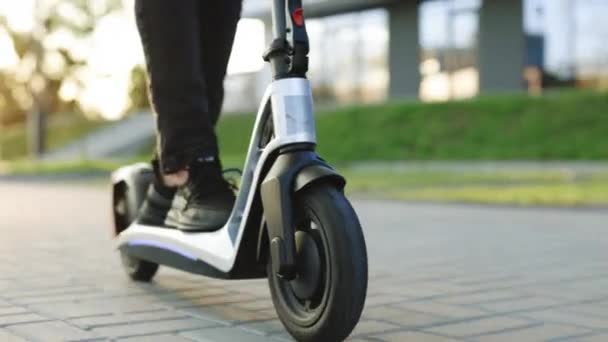 Close-up tiro de pernas masculinas montando em scooter elétrico fora na cidade urbana. Um tipo que usa mobilidade ecológica na cidade. Courier passeio de entrega de alimentos em scooter elétrico entregar cliente de ordem on-line — Vídeo de Stock