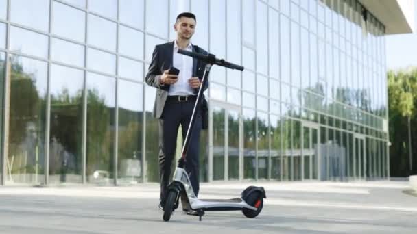 Jongeman gebruikt een elektrische scooter als een modern vervoermiddel in de stad. Een mannelijke zakenman benadert een elektrische scooter en het gebruik van mobiele telefoon app. Ecologisch vervoer — Stockvideo