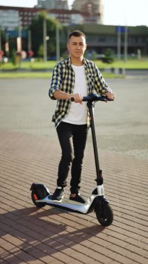 Hippi adam elinde elektrikli scooterla şehrin önünde dikiliyor. Çevre taşımacılığı. Modern kentsel alternatif ulaşım. Çevre dostu ulaşım
