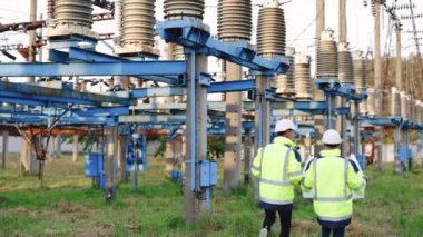 Sıcak giysili mühendisler dijital tablet bilgisayar kullanıyorlar. Elektrik santraline karşı yürümeyi tartışıyorlar.