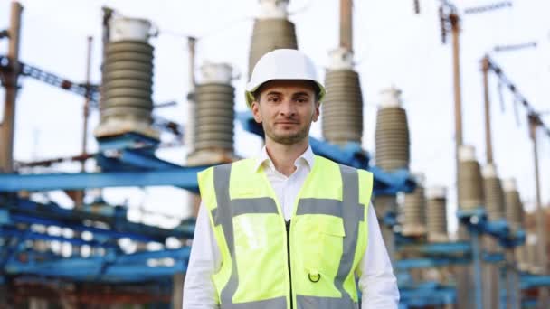 Retrato de engenheiro masculino feliz no capacete de proteção cruzando braços enquanto olha para a câmera. Bonito homem de uniforme sorrindo em pé na central elétrica de alta tensão — Vídeo de Stock