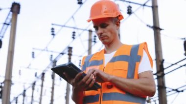 Elektrik kuleleri olan mühendis dijital tablet bilgisayar kullanıyor. Yüksek voltajlı elektrik pilonu olan elektrik mühendisi. İş konseptinde elektrik işçileri