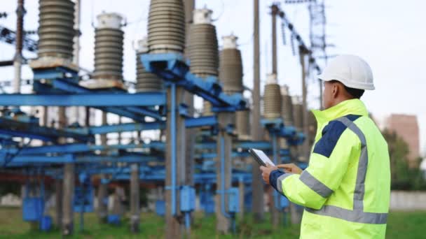 Elektrik işçisi, dijital tabletle çalışıyor. Kuleye yakın bir yerde elektrik var. Enerji sektörü teknoloji endüstrisi konsepti. Elektrik mühendisi tablet üzerinde çalışıyor.. — Stok video