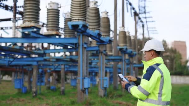 Elektrik işçisi, elektrik kulesinin yanında dijital tabletle çalışıyor. Enerji sektörü teknoloji endüstrisi konsepti. Elektrik mühendisi tablet üzerinde çalışıyor. — Stok video