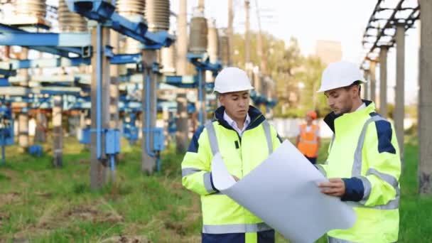 Dua insinyur listrik bertemu di dekat saluran listrik dan membahas rekonstruksi jalur tegangan tinggi pada rencana kertas. Konsep industri energi — Stok Video