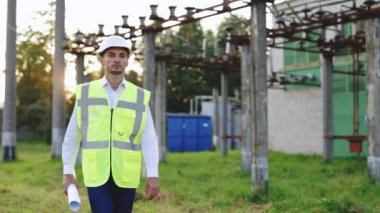 Hard Hat Holds Kâğıt Planı Giyen Profesyonel Fabrika İşçisi Modern Endüstriyel Elektrik İstasyonunda Yürüyor. Elektrik Mühendisi Kask ve Güvenlik Yeleği Giyiyor Elektrik Hatları Yakınlarında Yürüyor.