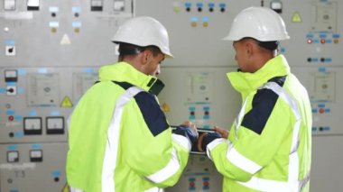 Elektrik mühendisleri kontrol panelini tabletle kontrol ediyorlar. Elektrik endüstrisi, elektrik enerjisi üretim konsepti. Yüksek voltaj güç istasyonu.
