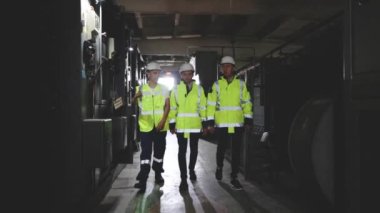 Elektrik santralinden geçen üç mühendis takımı. Koruyucu miğfer ve üniformalı elektrik mühendisleri kontrol paneli yüksek voltaj güç istasyonunu kontrol ediyor.