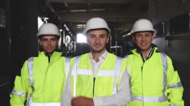 Profesyonel telekomünikasyon endüstrisi mühendislerinin portresi gülümsüyor ve kameraya bakıyor. Güvenlik üniforması giyen işçiler ve odaklanmamış arka planda sert şapka takanlar