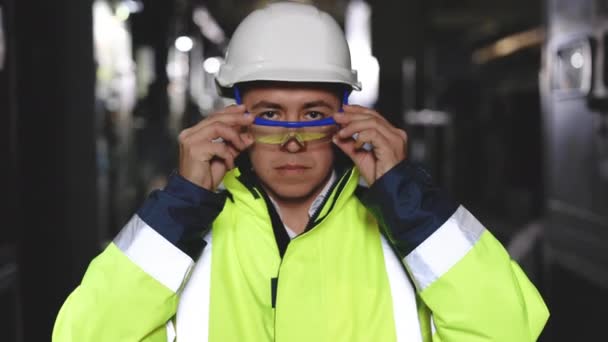 Primer plano del ingeniero serio profesional que mira la cámara, lleva uniforme de seguridad y gafas de pie en la fábrica de la industria pesada lista para fabricar trabajos durante la soldadura de metal por parte del personal — Vídeos de Stock