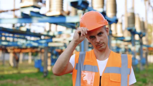 Retrato de un joven ingeniero profesional de la industria pesada que usa chaleco de seguridad, poniéndose un sombrero duro. En segundo plano Gran central eléctrica desenfocada. Moción lenta en 4k UHD. — Vídeo de stock