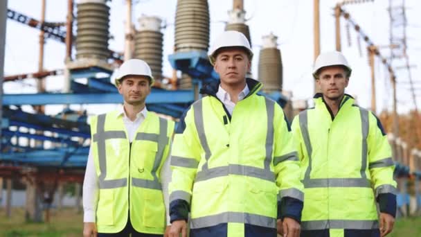 Retrato atractivo tres hombres ingenieros trabajadores con uniforme de seguridad y sombrero duro cruzando brazos y mira a la cámara. Sitio industrial. Retrato. Arquitecto. Uniforme. — Vídeo de stock