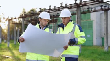 Endüstri Mühendisleri Grubu, Endüstriyel Üretim Fabrikasındaki bilgi ve güvenlik sistemini kontrol etmek için planlar üzerinde tartışıyorlar. Gün batımında kağıt işleriyle konuşan iki işçi..