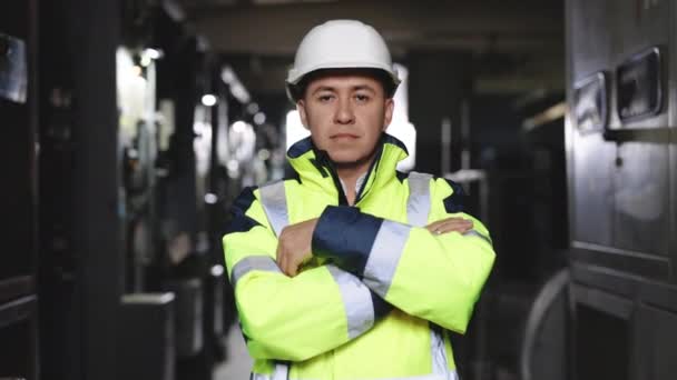 Portret van een zelfverzekerde ingenieur met een veiligheidsvest en een helm op in de elektrische controlekamer. Betrouwbare houding van de werknemer in veiligheid uniform kijken naar de camera — Stockvideo