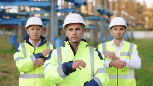 Multinational expert engineer team crossing their arms confidently, smart teamwork standing near industry power factory. Industrial site. Portrait. Uniform. — Stock Video