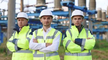 Koruyucu kask takan ve kollarını kavuşturan genç çoklu etnik gruptan erkek teknisyen portre ekibi. Takım çalışması kameraya poz veriyor. Yavaş çekim