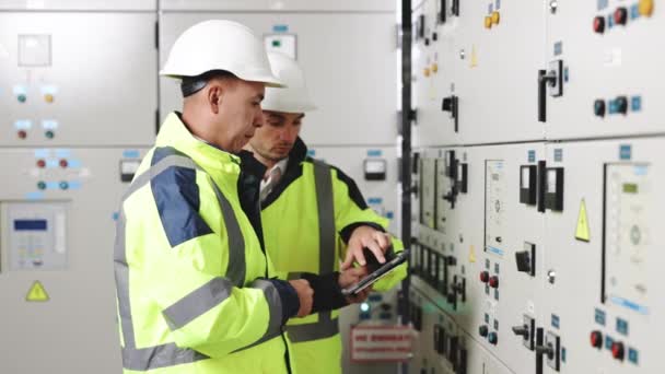 Ingenieros eléctricos comprobando tablero del panel de control con la tableta. Central eléctrica de alto voltaje. Ingenieros eléctricos de pie cerca de la caja térmica del panel solar — Vídeos de Stock