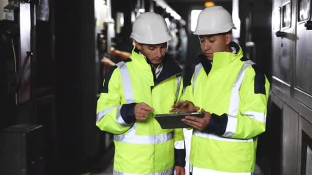 Männliche Elektrotechniker mit harten Hüten diskutieren über ein neues Projekt, während sie Tablet-Computer benutzen. Sie treffen kalkulierte technische Entscheidungen. Sie arbeiten in der Elektrizitätsfabrik — Stockvideo