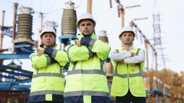 高圧電気ラインの背景と安全制服とハード帽子を身に着けている労働者。ポートレートエンジニアや建築家が腕を渡ってカメラを見る — ストック動画
