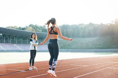 Spor salonunun bir parçası olarak kişisel antrenörüyle ip atlayan beyaz bir kadın. Güzel vücutlu, sportif bir kadın stadyumun spor pistinde ip atlıyor. Güç ve kardiyo egzersizi.