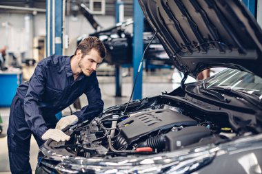 Otomobil tamirhanesi. Tamirci araba motorunu inceliyor.