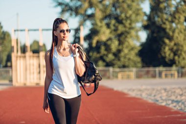 Spor çantalı genç bir kadın spor sahasında yürüyor.