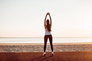 Sabahın erken saatlerinde spor sahasında ısınma egzersizleri yapan genç bir kadın.