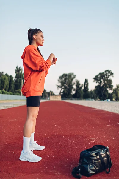 Mujer joven haciendo ejercicios de calentamiento en el campo de deportes temprano en la mañana — Foto de Stock